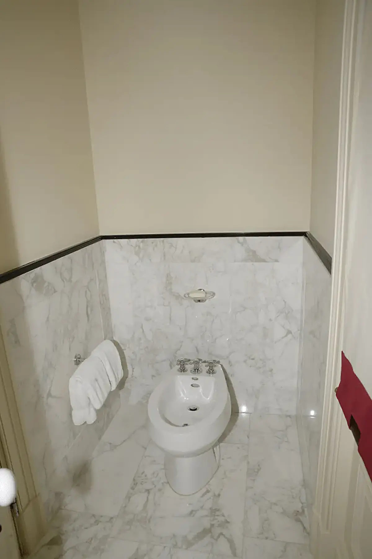 Salle de bains: EFTA00000241 - White bidet in a marble-walled bathroom with folded towels on the wall and