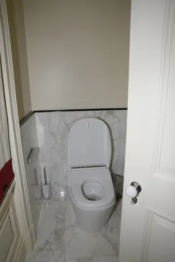 Badezimmer: EFTA00000242 - White toilet in a small bathroom with marble tiles a trash can and a door p