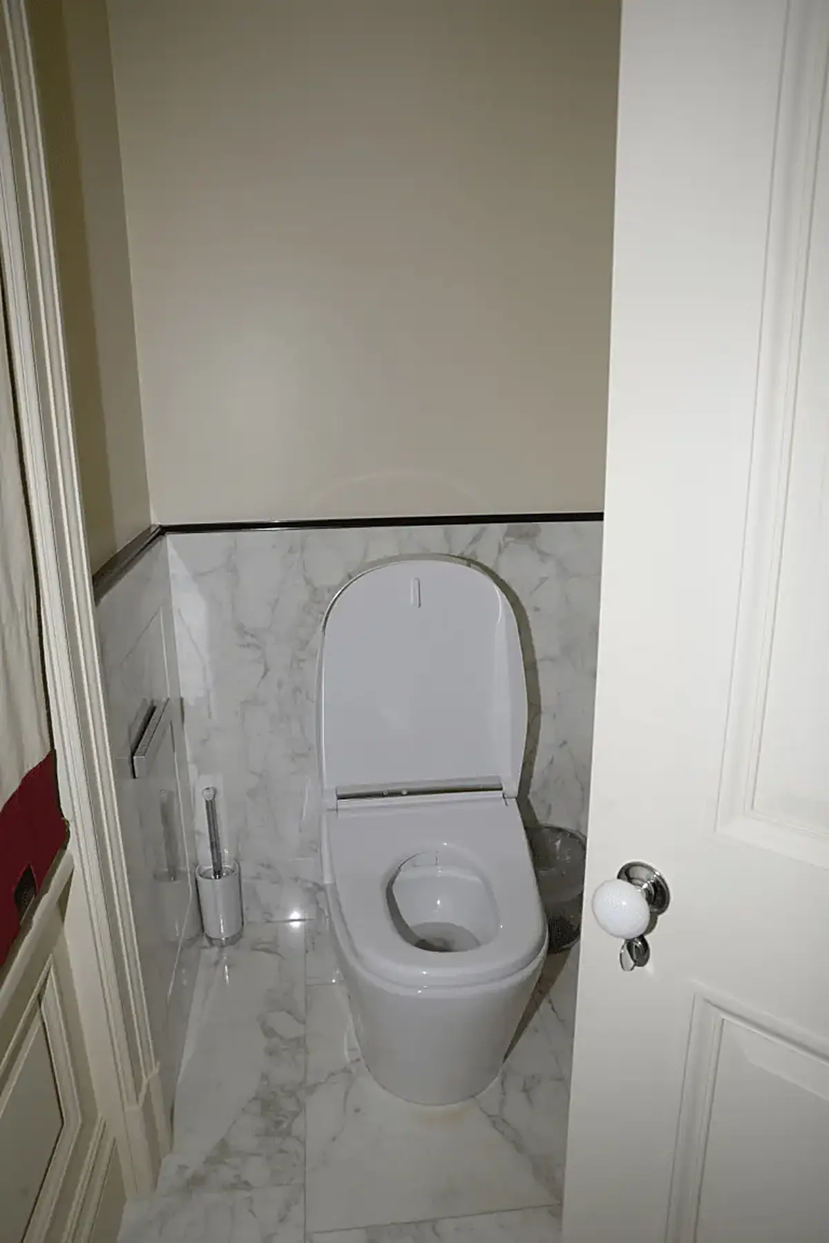 Ванная: EFTA00000242 - White toilet in a small bathroom with marble tiles a trash can and a door p