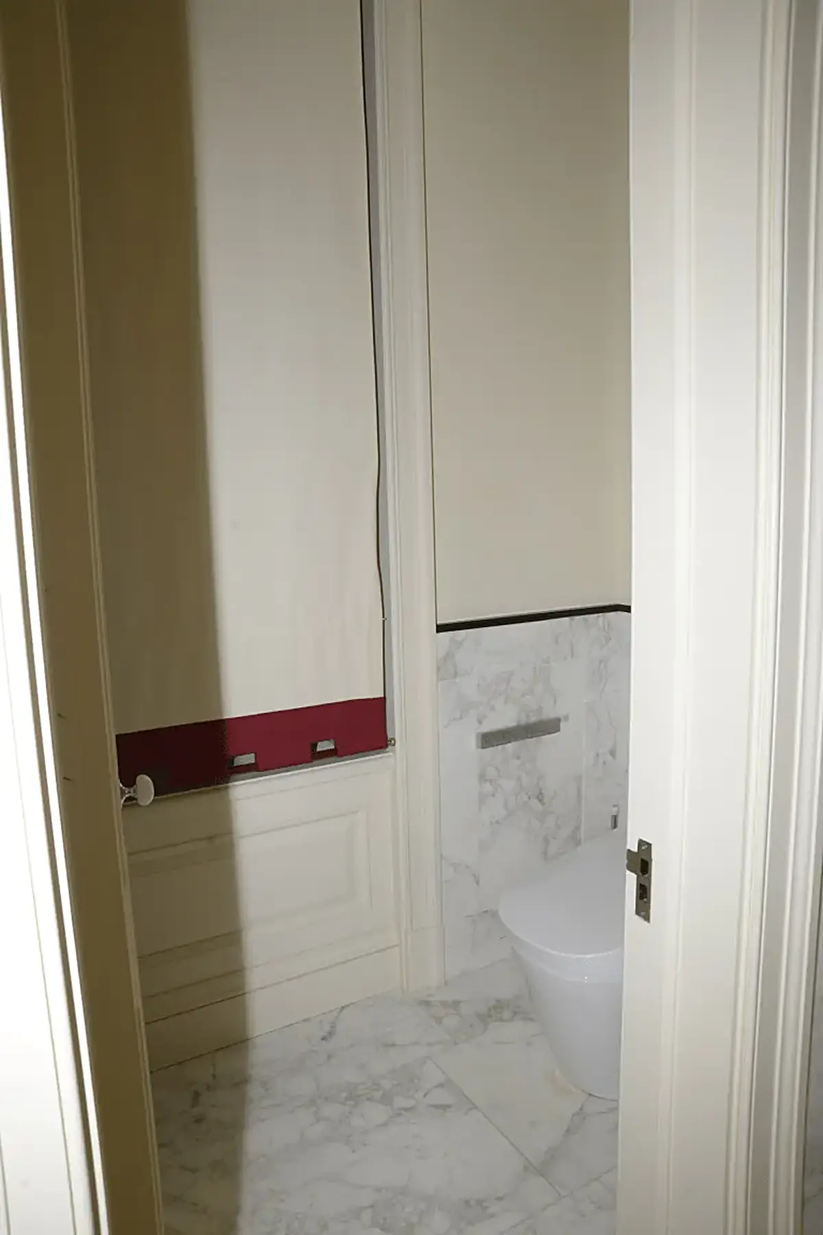 Badezimmer: EFTA00000604 - Bathroom with white marble flooring a modern toilet and a red trim on the w