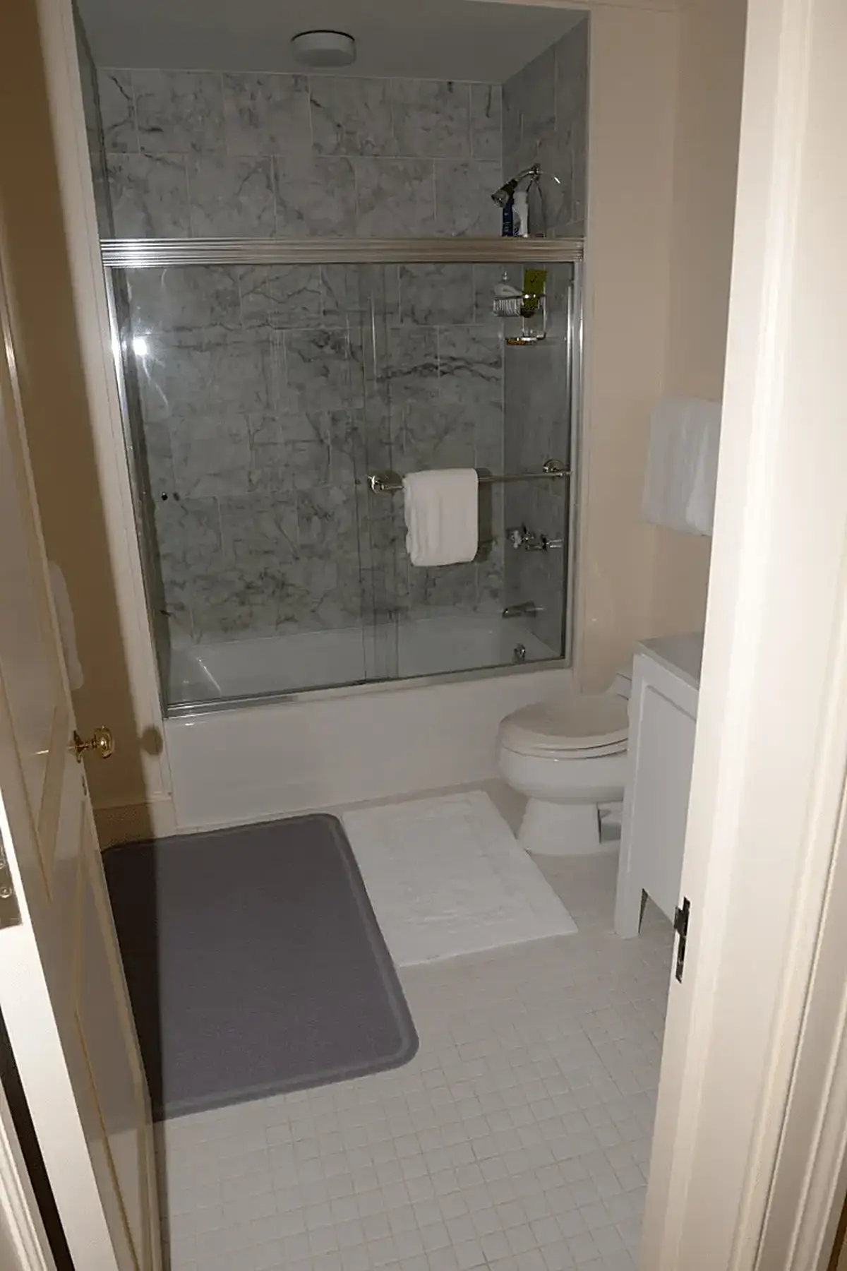 Ванная: EFTA00001163 - Small bathroom featuring a shower with marble tiles white fixtures and a gr