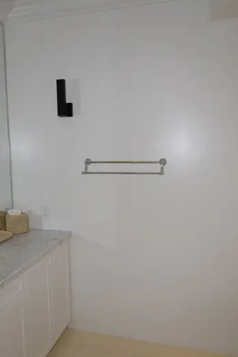 Badezimmer: EFTA00001602 - White bathroom with marble countertop silver towel bar and black wall sconc