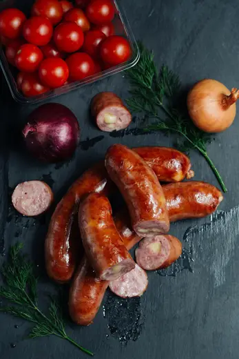 Kitchen: Sausages surrounded by fresh vegetables on a dark countertop ready for preparation