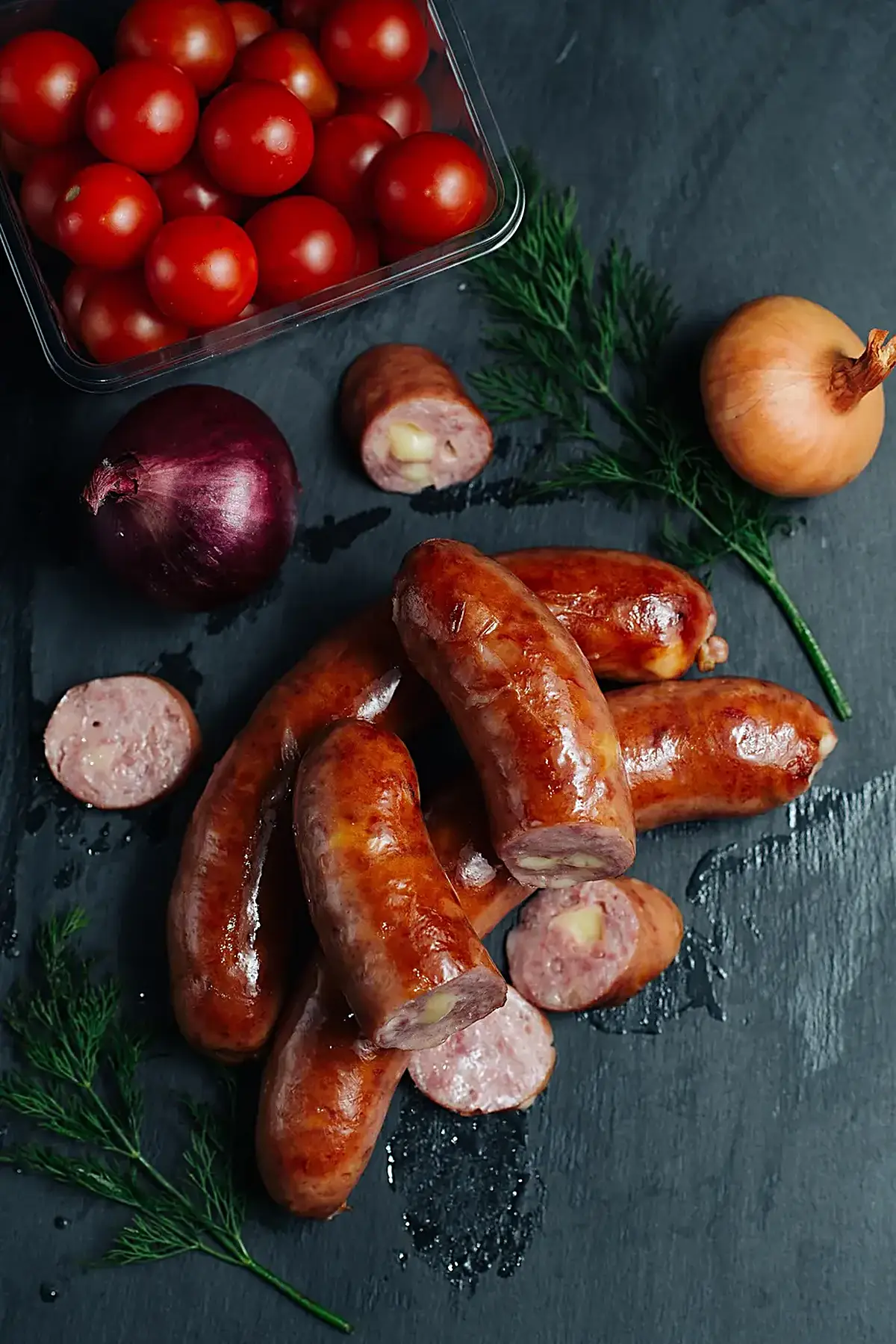 Küche: Sausages surrounded by fresh vegetables on a dark countertop ready for preparation