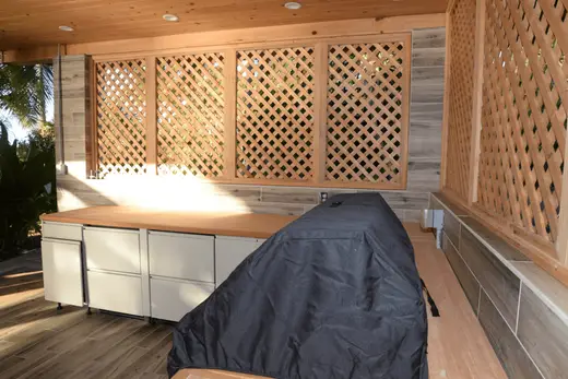 Kitchen: EFTA00002811 - Wooden lattice wall and countertop surround a covered grill in a sunny outd
