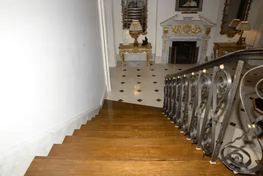 Scala: EFTA00000822 - Grand wooden staircase leads to an opulent hallway featuring ornate iron ra